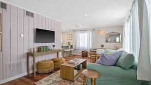 Un salon comprenant un téléviseur, un canapé, une table basse et un coin repas avec des chaises.