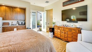 Ein Schlafzimmer mit einem großen Bett, einem Schminktisch, einem Fernseher und einer Küchenzeile mit Schränken und einer Mikrowelle.