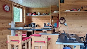 Een compact houten vakantiehuisje met een kitchenette, een eethoek met krukken, en een werkplek met een laptop.