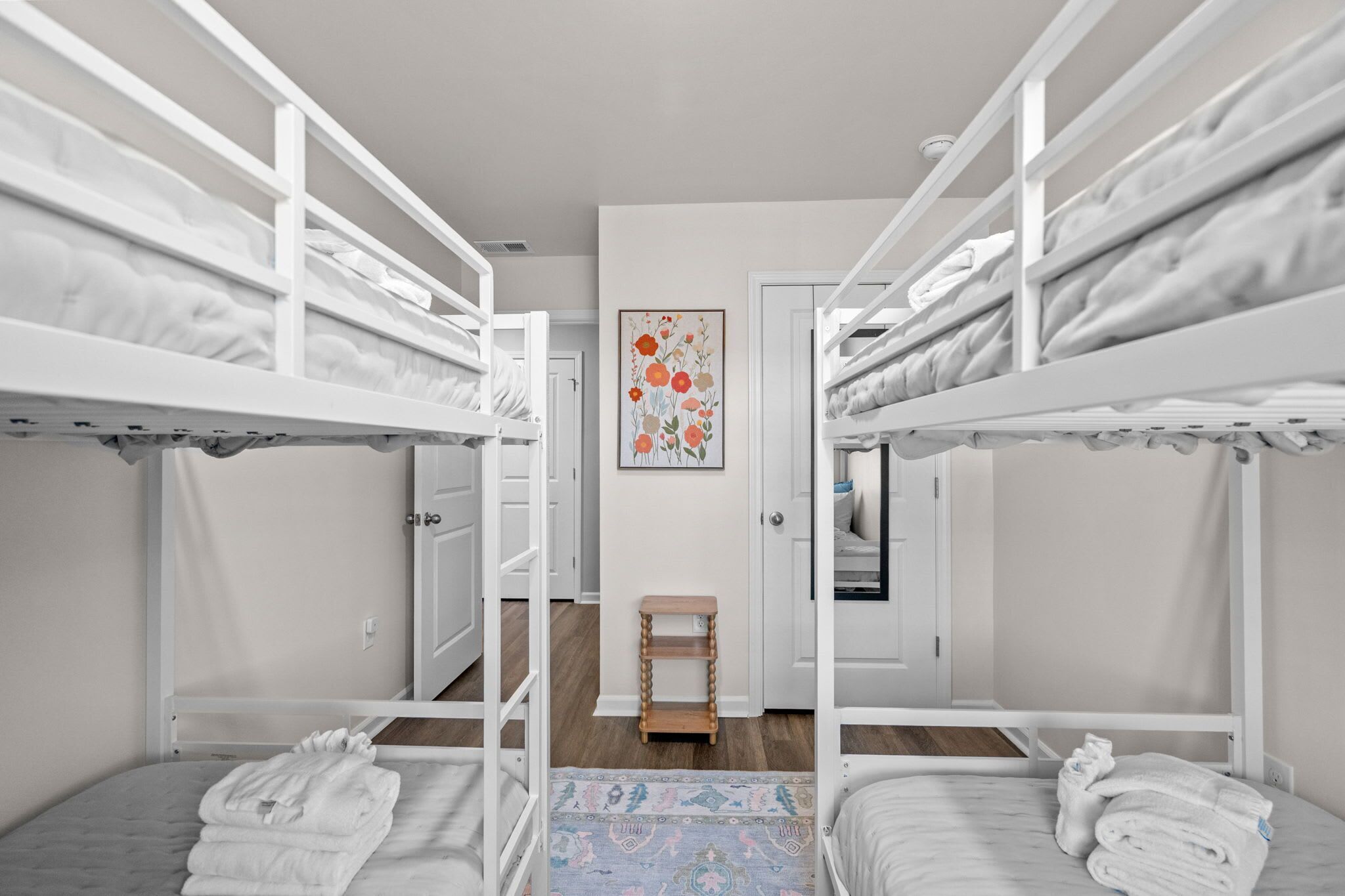 A room with bunk beds, a small wooden stool, and a framed floral artwork on the wall.