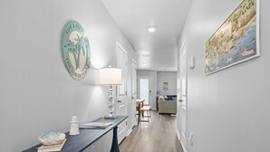 A hallway with a dark blue console table, a white lantern, and a decorative plate with palm trees. - Tide And Tee Ping Pong Golf Cart By Beach Star (Surfside Beach)