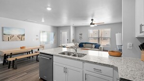 A modern kitchen with granite countertops, white cabinetry, and a built-in dishwasher. - Tide And Tee Ping Pong Golf Cart By Beach Star (Surfside Beach)
