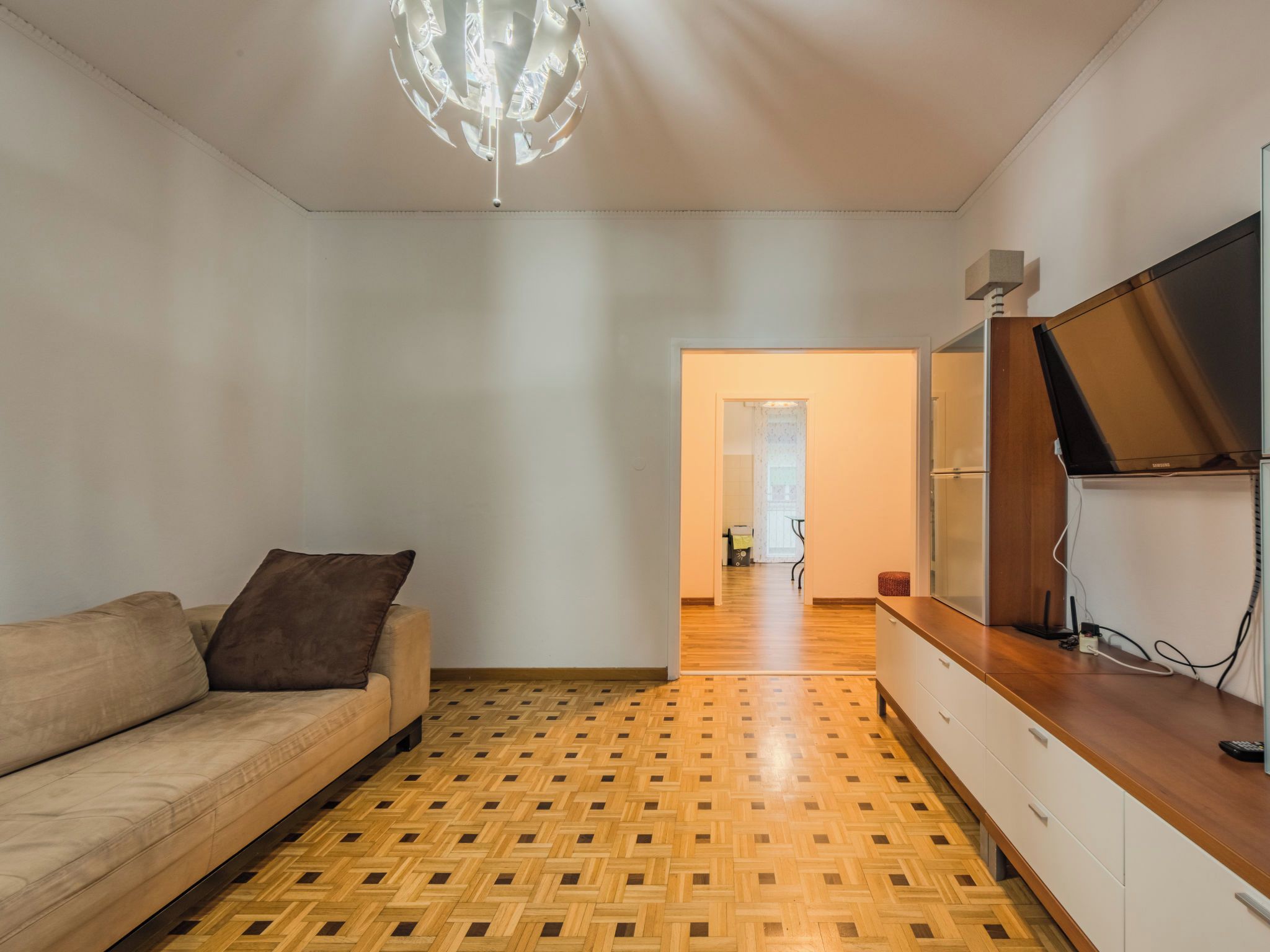En moderne stue med en sofa, trægulv i parket, et fjernsyn og en loftlampe.
