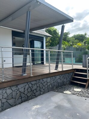 Um terraço moderno ao ar livre com parede de pedra, guarda-corpo de metal e escadaria para uma área coberta.