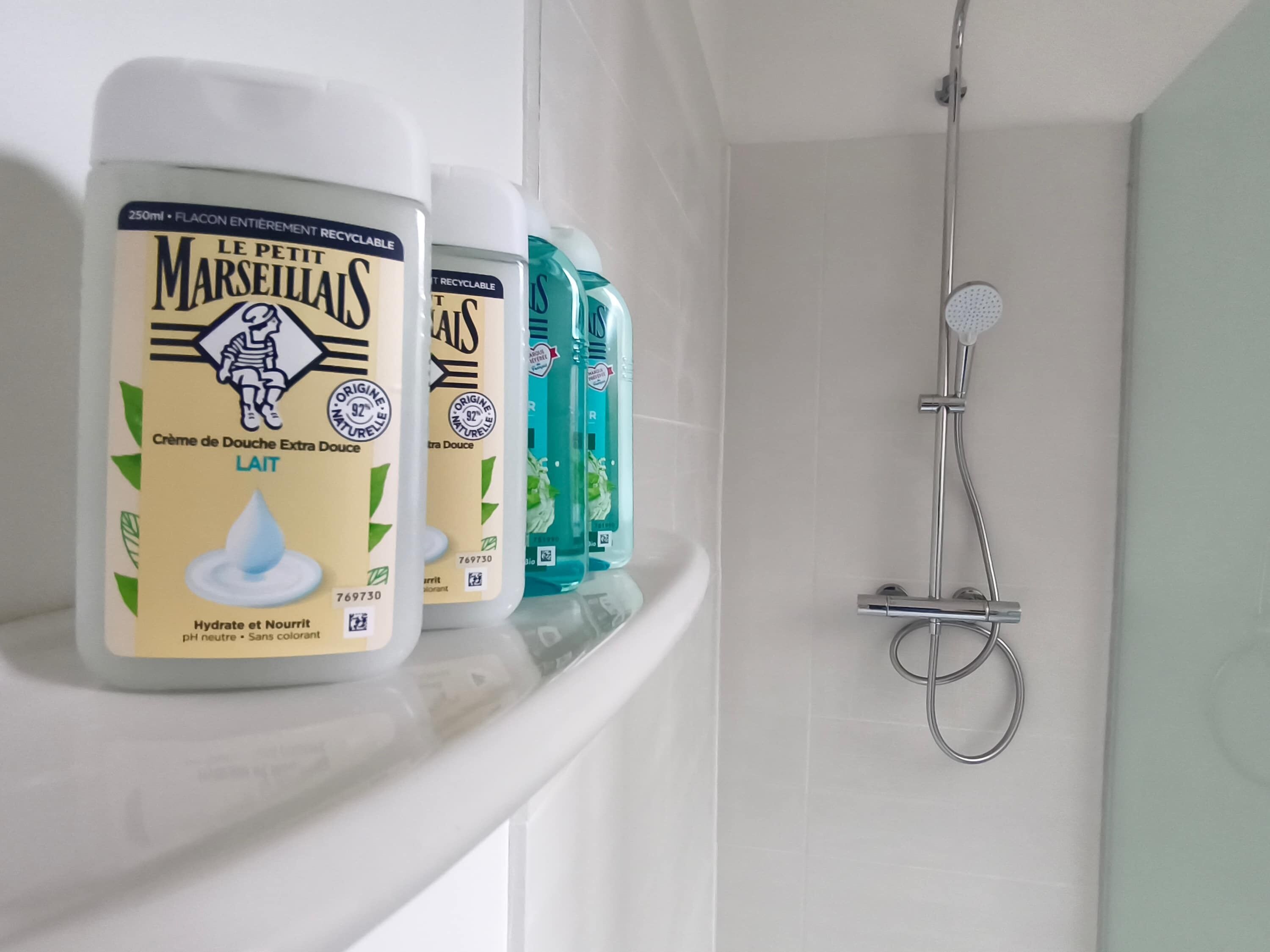 Estante de baño con botellas de jabón corporal y acondicionador Le Petit Marseillais.