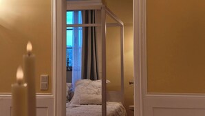 A bedroom with a four-poster bed, a window with curtains, and a bedside table with a lamp. - Elegance & Charm in Château – Suite Marie Thérèse (Malberg)