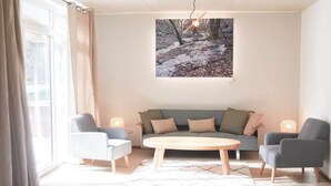 Moderni olohuone, jossa on sohva, kaksi nojatuolia, sohvapöytä ja suuri taulu seinällä.