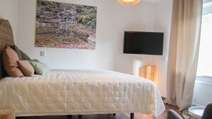 Een slaapkamer met een bed, een schilderij, een televisie en een lamp.