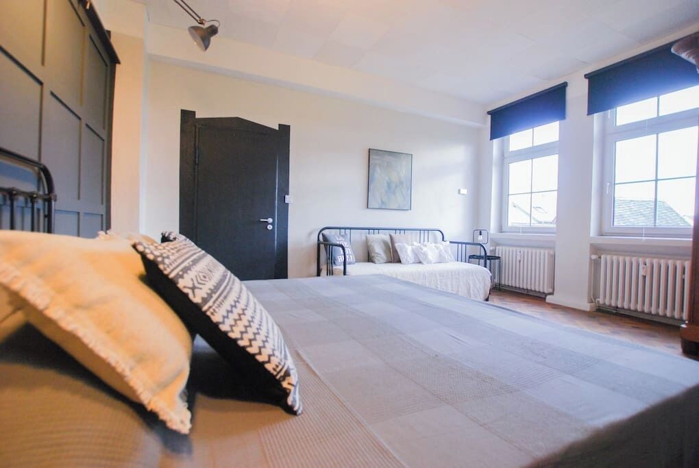 Une chambre avec deux lits, une porte sombre, un radiateur et une fenêtre donnant sur un paysage agréable.