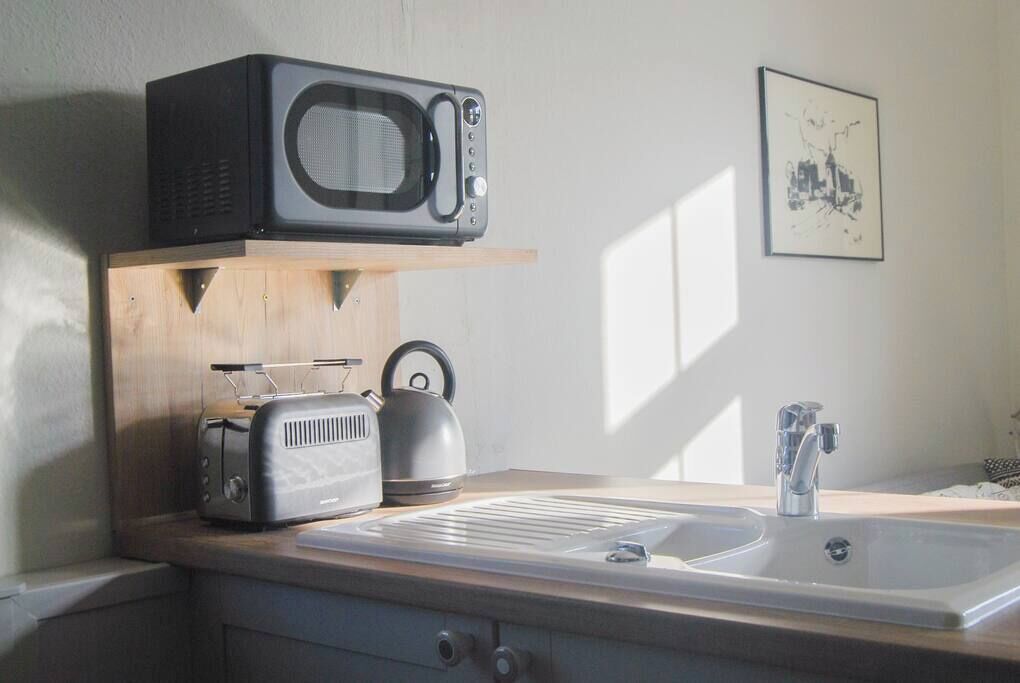 A kitchen with a microwave, toaster, kettle, and sink.