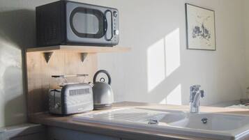 A kitchen with a microwave, toaster, kettle, and sink.