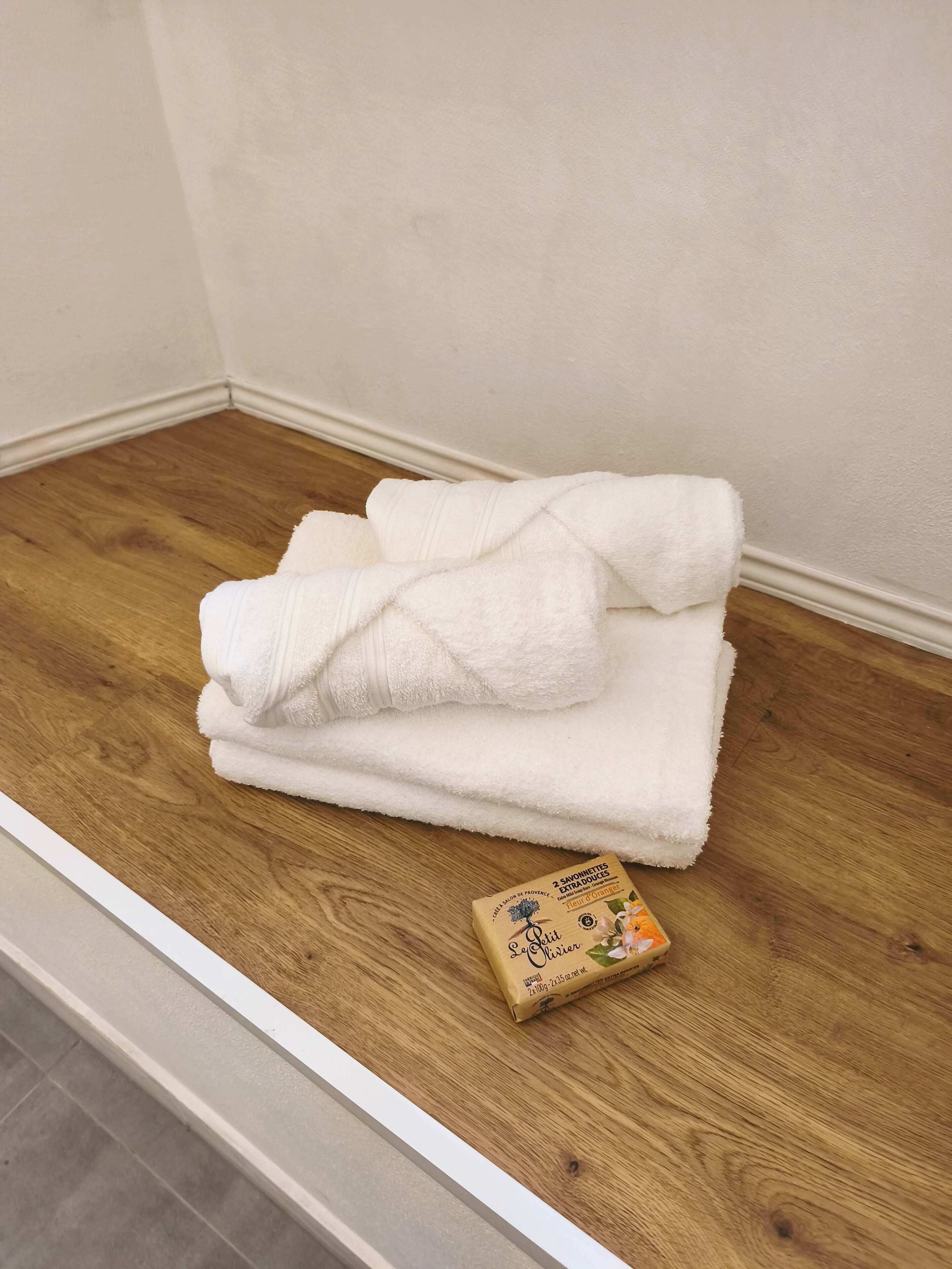 A stack of white towels on a wooden floor next to a white wall.