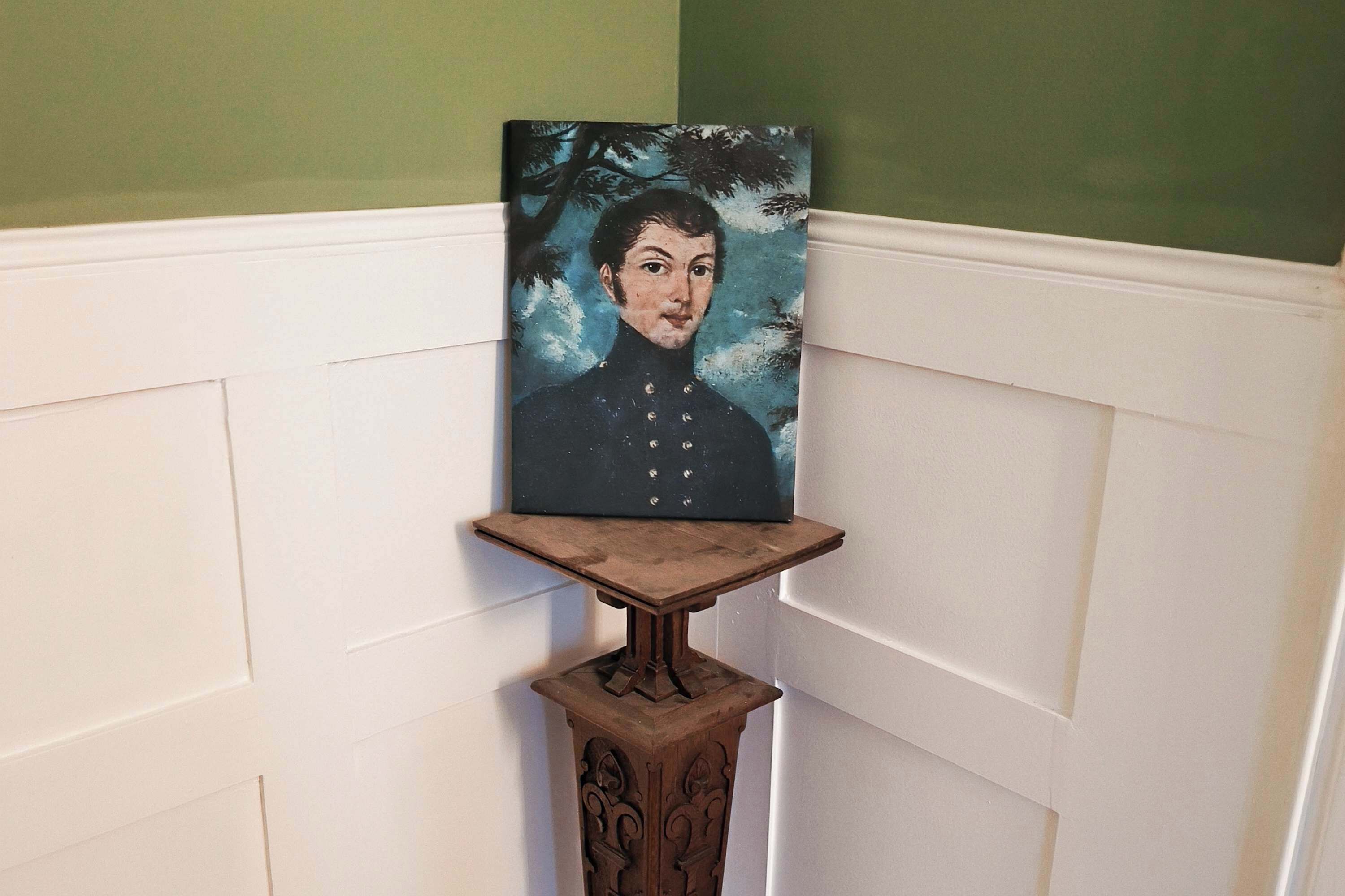 A framed portrait on a wooden stand against a white wall with paneling.