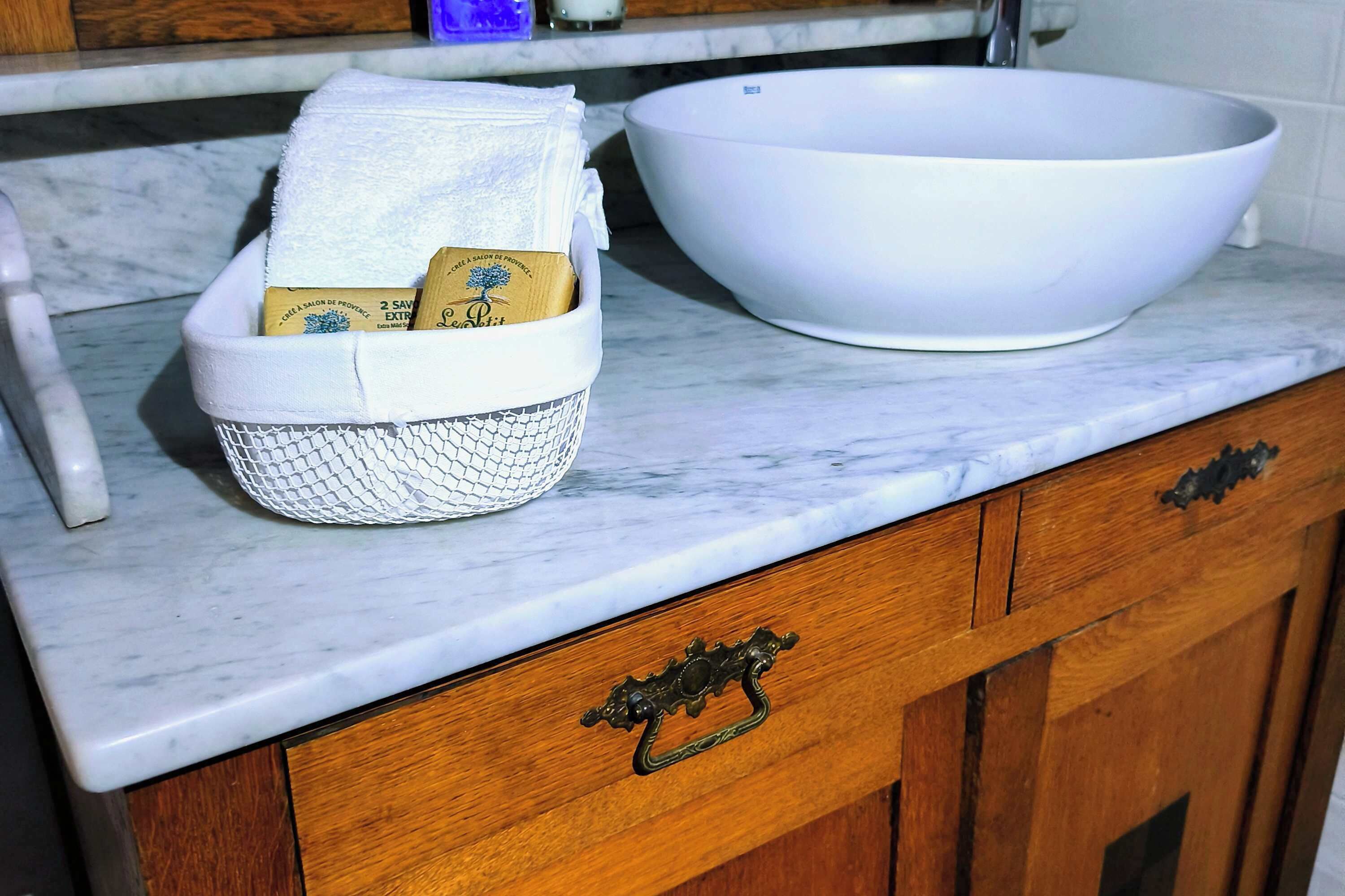 A kitchen counter with a white sink and a basket containing a towel and a bar of soap.