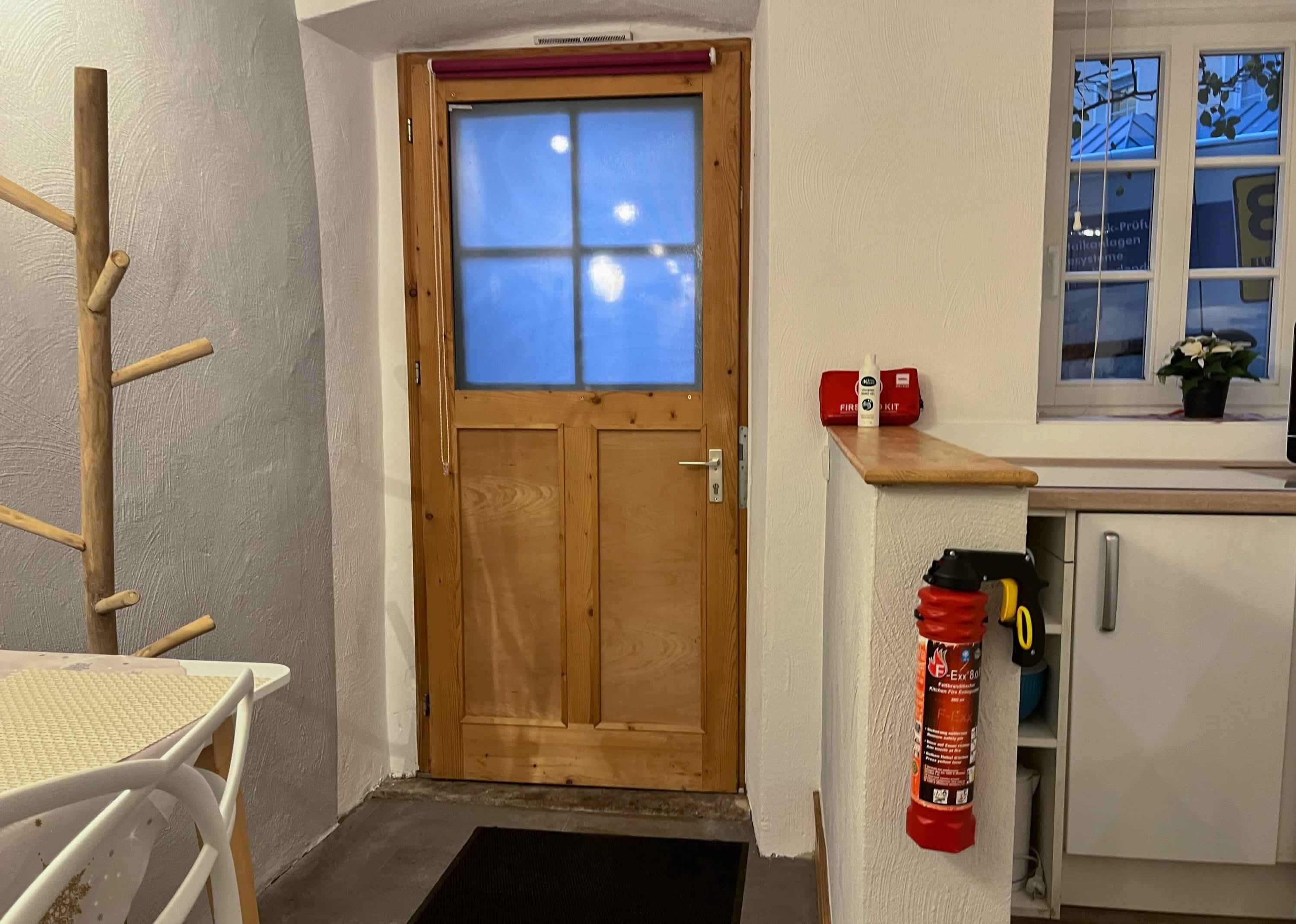 En trædør med et vindue, en brandslukker ophængt på væggen, et lille bord og et skab.