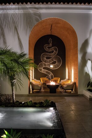 A modern lounge area with a central fire feature, comfortable seating, and a decorative wall with a spiral design.