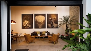 Una sala de estar moderna con un conjunto de sofá, una mesa de centro y un comedor con sillas y una mesa. Hay tres obras de arte enmarcadas en la pared y una planta en maceta en la esquina.