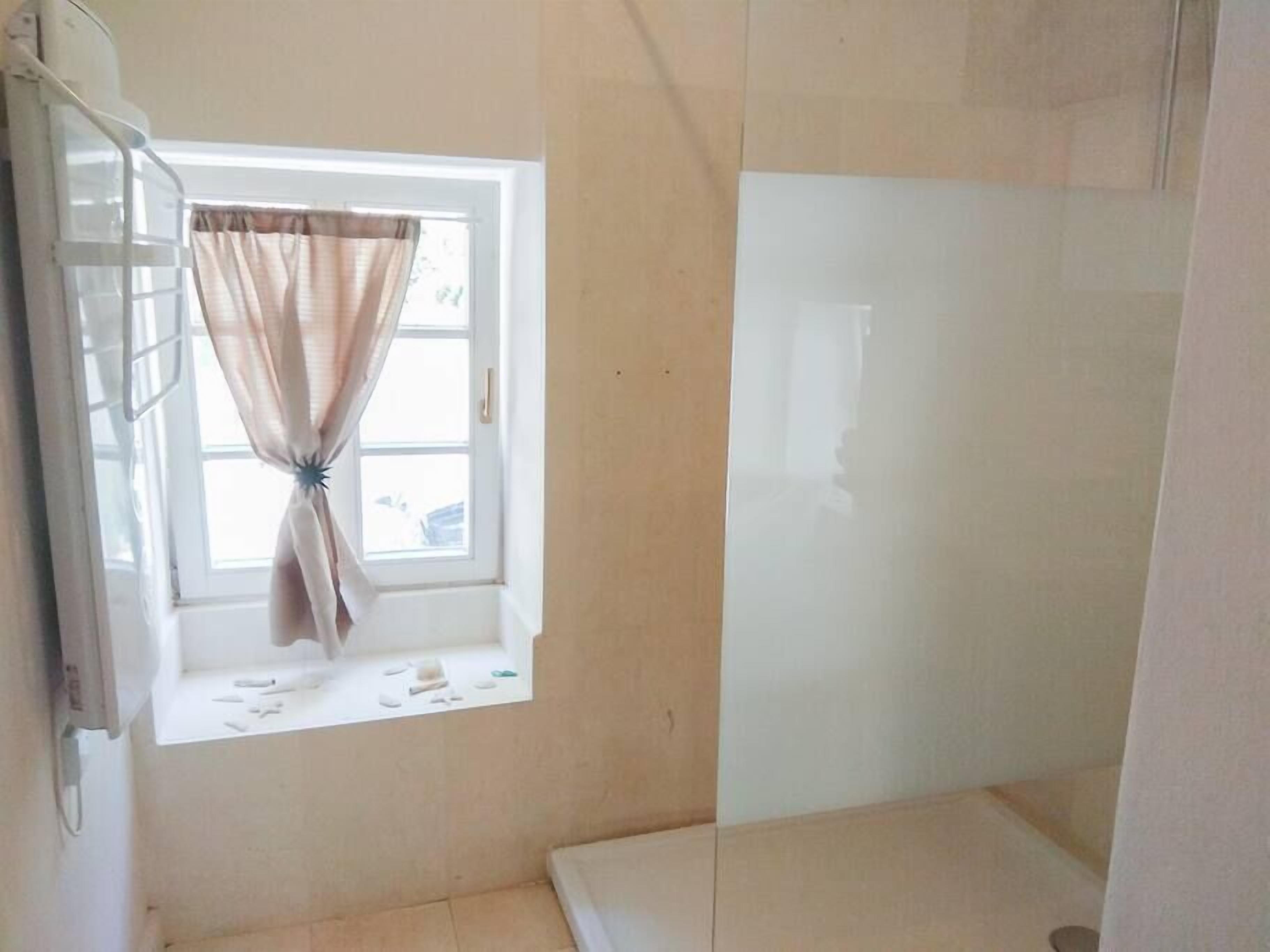Un baño con ventana, zona de ducha y retrete.