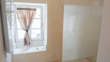 Un baño con ventana, zona de ducha y retrete.