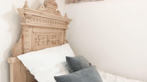 A bed with a carved wooden headboard, white and grey pillows, and a white bedspread. - Living in history: Heidi Braun Cottage (Dudeldorf)