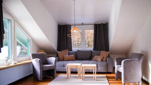 A modern loft bedroom with a sloped ceiling, a grey sofa set, two armchairs, a wooden coffee table, and a hanging light fixture. - Small timeout, spring water shower, thermal spa incl. (Traben-Trarbach)