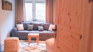 A cozy living room with a grey sofa, two ottomans, a wooden coffee table, and a window with curtains.
