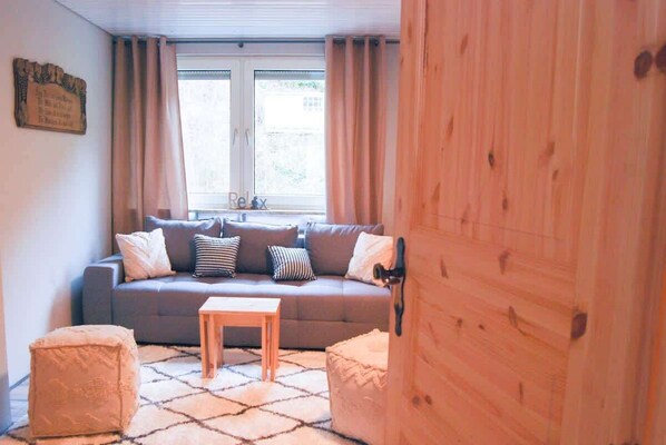 A cozy living room with a grey sofa, two ottomans, a wooden coffee table, and a window with curtains.