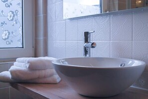 A bathroom with a white vessel sink, a mirror, and a window with floral blinds.