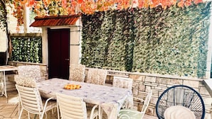 An outdoor patio with a table set for dining, surrounded by chairs, and a decorative wall with foliage. - Spacious Stone Villa With Sea Views (Dubrovnik)