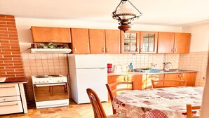 A kitchen with wooden cabinets, a stove, a refrigerator, and a dining table with chairs. - Spacious Stone Villa With Sea Views (Dubrovnik)