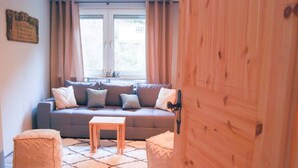 Una sala de estar acogedora con un sofá gris, dos otomanas, una mesa de centro de madera y una ventana con cortinas.