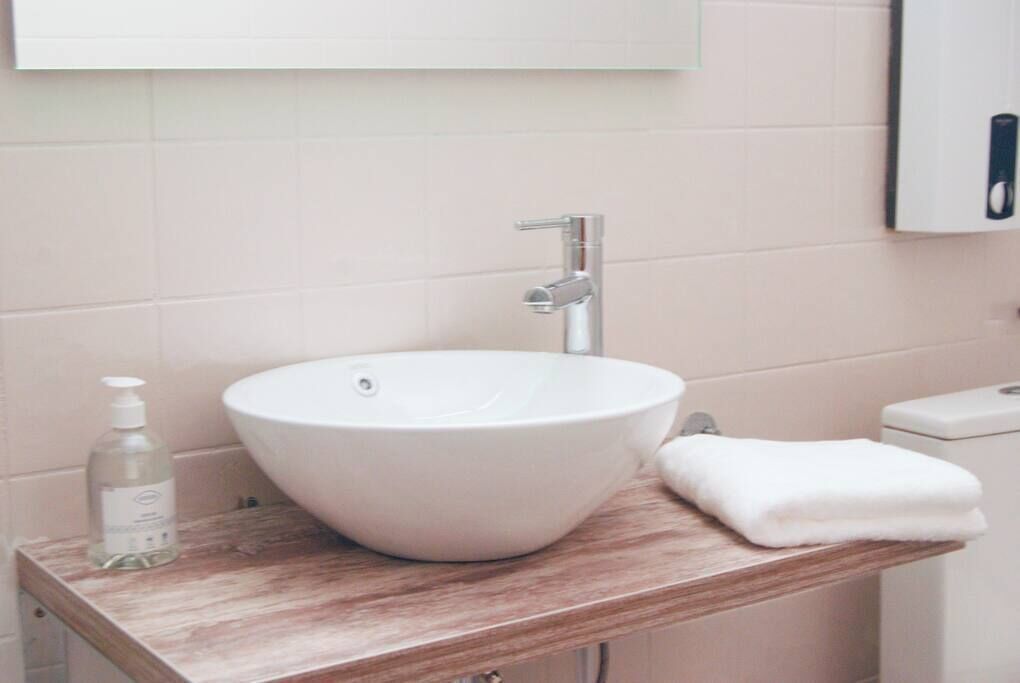 Une salle de bain avec un lavabo blanc, un plan de toilette en bois, un flacon de savon liquide et une serviette blanche.