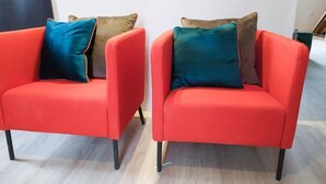 Deux fauteuils rouges avec des pieds noirs et des coussins de couleurs différentes.