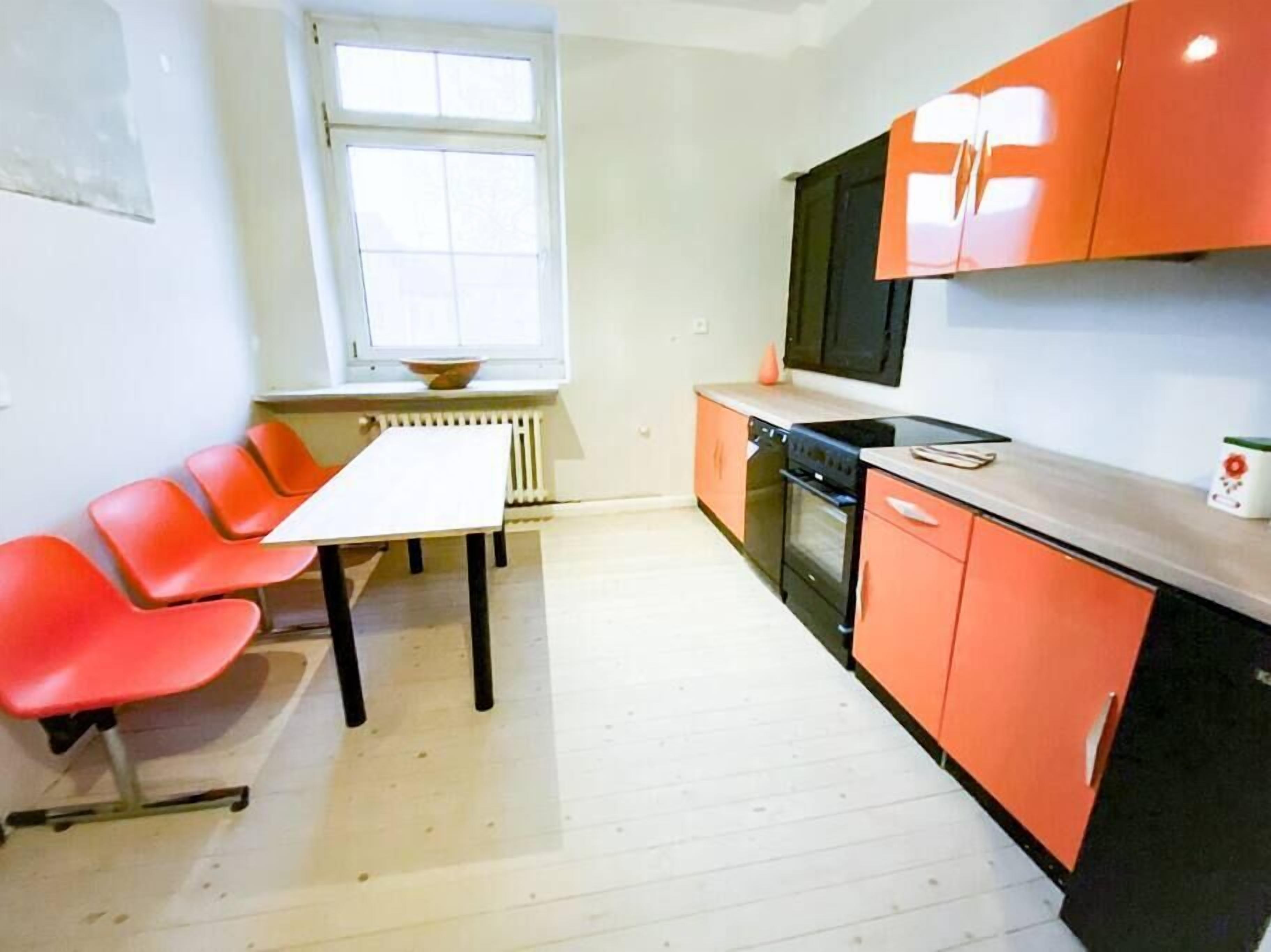 Une cuisine avec des meubles de couleur orange, un plan de travail blanc, une cuisinière noire et une fenêtre au-dessus de l’évier.