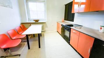 Une cuisine avec des meubles de couleur orange, un plan de travail blanc, une cuisinière noire et une fenêtre au-dessus de l’évier.