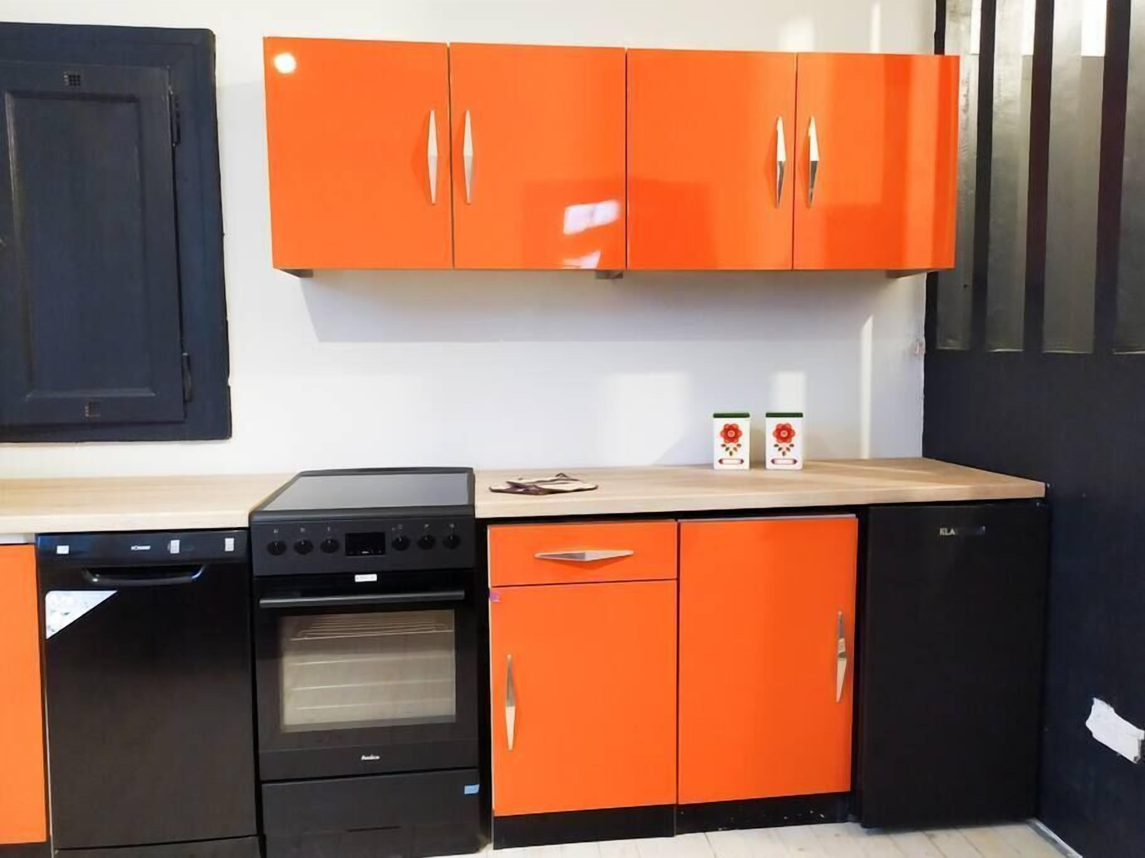 Eine Küche mit schwarzen und orangefarbenen Schränken, einem Geschirrspüler, einem Backofen und einem Herd.