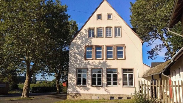 Une maison à deux étages, dotée d’un toit à forte pente, de nombreuses fenêtres et d’une clôture en bois au premier plan.