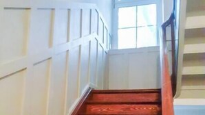 Un escalier en bois, avec des panneaux blancs sur les murs et une fenêtre en haut.