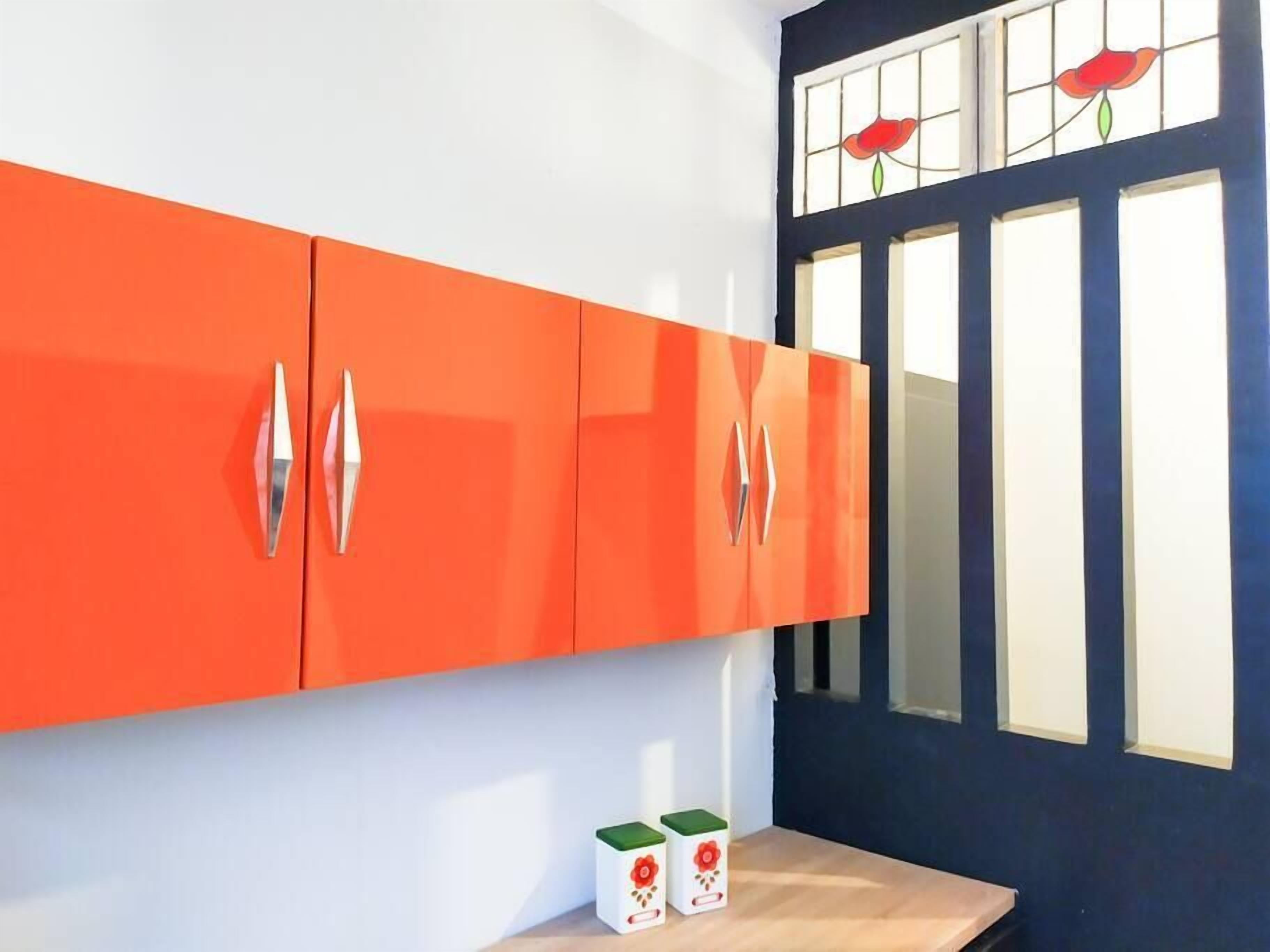 Una cocina con gabinetes naranja y una puerta azul con vidrieras.