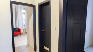 Un couloir au plancher de bois mène à une pièce où se trouve un canapé rouge et une fenêtre avec des rideaux.