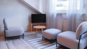 A modern living room with a television on a wooden stand, two grey armchairs, a small round table, and a striped rug on a wooden floor. - Quiet, spacious room, priv. Bathroom, spring water (Traben-Trarbach)