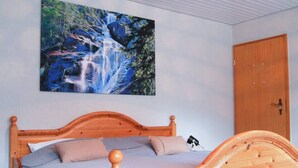 A wooden bed with a headboard, a wall-mounted painting of a waterfall, and a wooden door. - Quiet, spacious room, priv. Bathroom, spring water (Traben-Trarbach)
