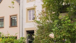 A building with multiple windows and a door, surrounded by lush greenery and flowering plants.