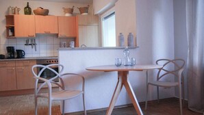A compact kitchen with wooden cabinets, a gas stove, and two white chairs around a small round table. - Relax and comfort, spring water shower, thermal spa incl. (Traben-Trarbach)