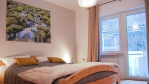 A bedroom with a wooden bed, a large window with a view of trees, and a painting on the wall. - Relax and comfort, spring water shower, thermal spa incl. (Traben-Trarbach)