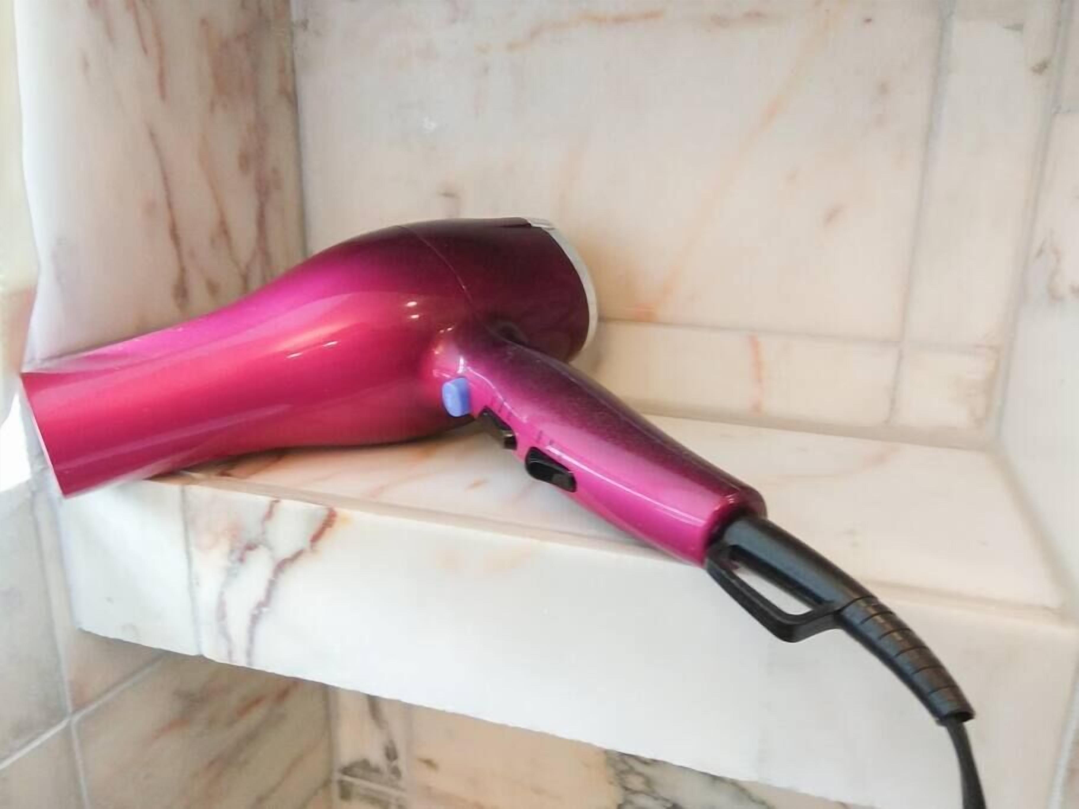 Ein pinker Haartrockner ist in eine weiße Steckdose gesteckt.