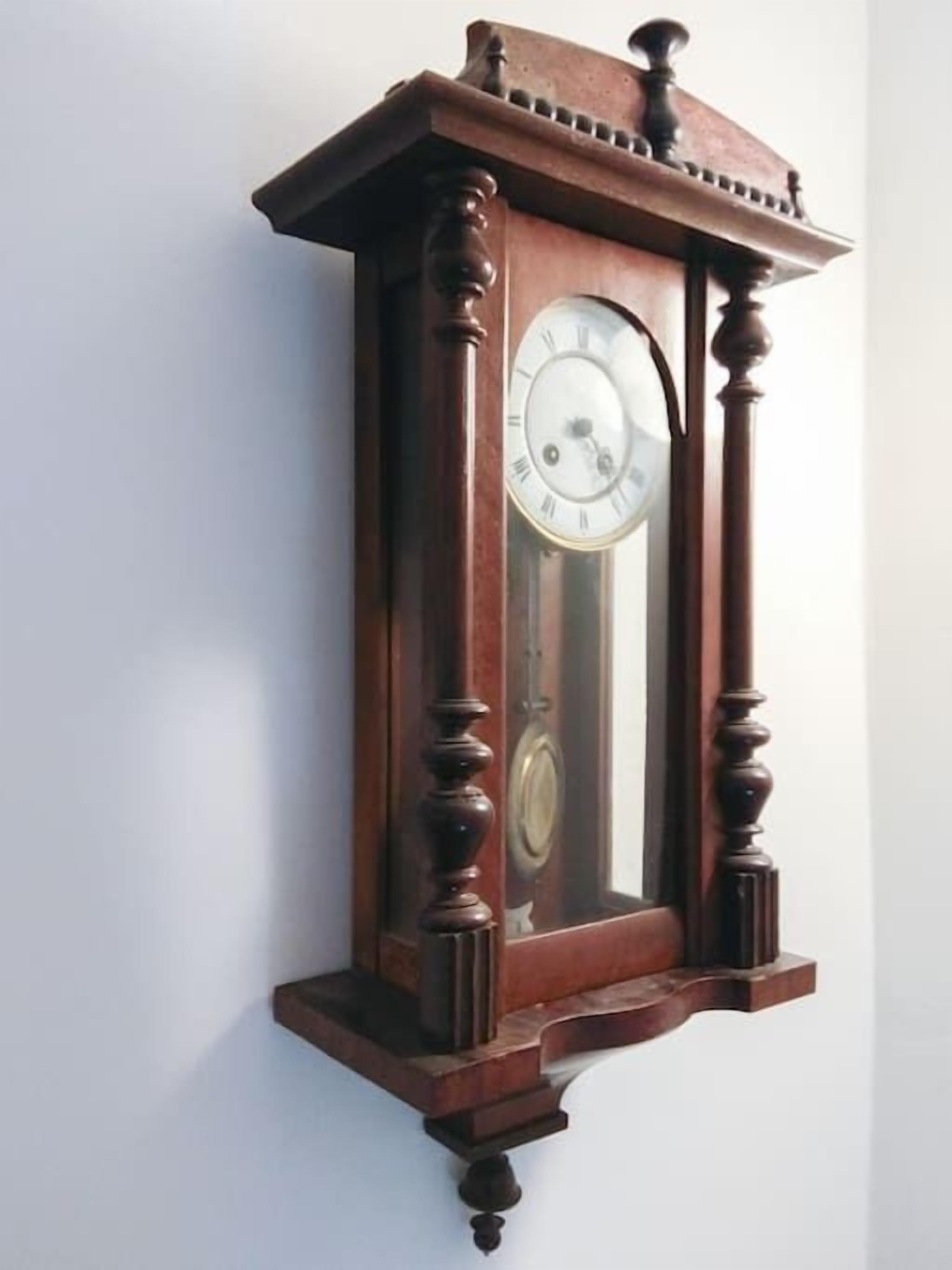 A wall-mounted wooden grandfather clock with a pendulum and Roman numerals.