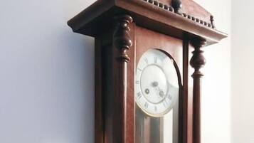 A wall-mounted wooden grandfather clock with a pendulum and Roman numerals.