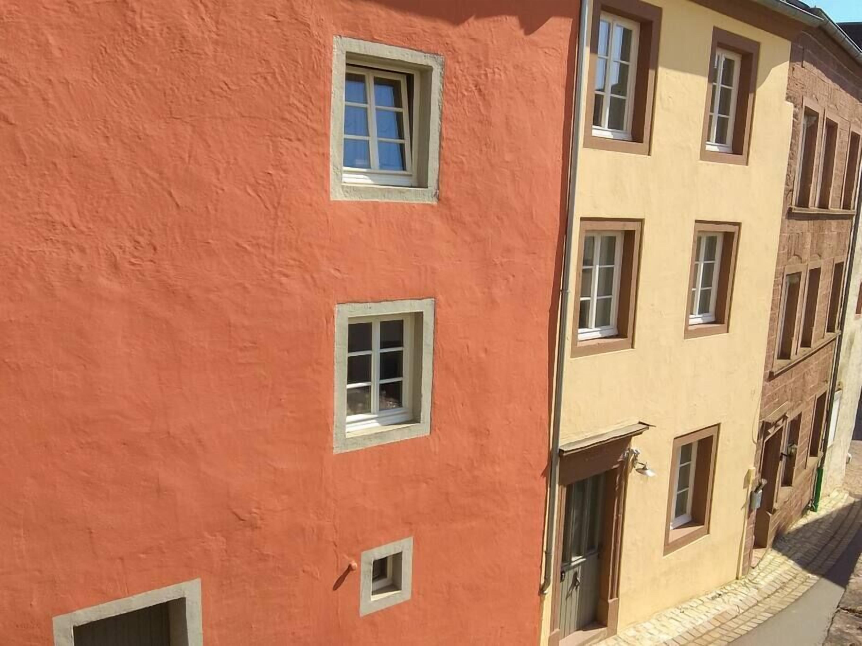 Un immeuble à plusieurs étages, doté d’une façade rouge et d’étages supérieurs de couleur beige, avec de nombreuses fenêtres et une porte bien visible.