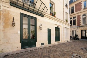 A building with a cobblestone street, green doors, and a balcony with a metal railing. - Superbe Flat With AC Champs Elysees Av Montaigne (Paris)